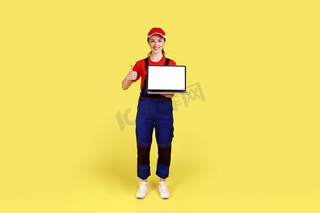 女工人站着拿着带有广告空白屏幕的笔记本电脑，竖起大拇指。