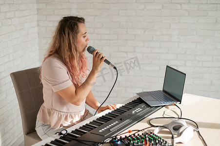 一位女士在家中使用笔记本电脑和键盘伴奏录制声乐课程。