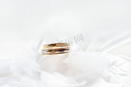 白色丝绸织物上镶有钻石的金色结婚戒指。