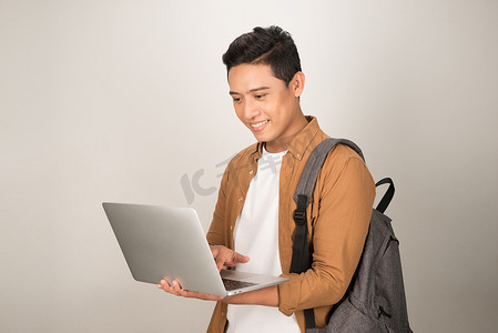 一个英俊的年轻学生使用笔记本电脑和背着白色背景中突显的背包