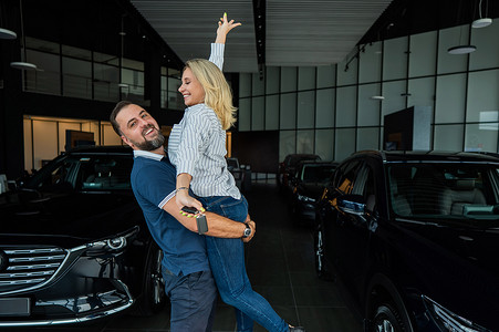 拥抱客户摄影照片_幸福的白人夫妇在汽车经销店购买新车时拥抱。
