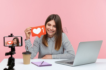情绪化的年轻女性坐在粉红色背景的办公室里工作。