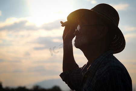 金色高级摄影照片_戴着帽子的高级农民的轮廓在日落时望向远方，在金色的天空背景上做一个心形。