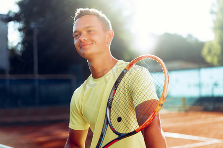 网球少年摄影照片_在红土场上，拿着网球拍站在网边的青年少年