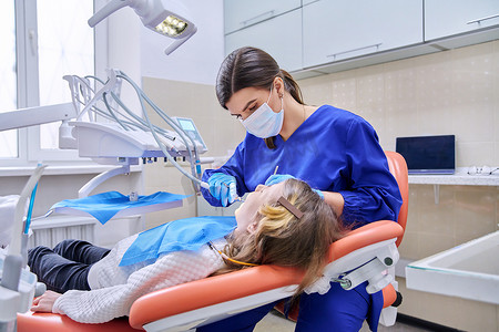 麻醉摄影照片_女医生牙医使用麻醉为一名女童治疗牙齿。