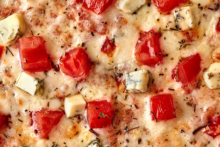比萨饼的宏观照片，配西红柿、戈贡佐拉、融化的马苏里拉奶酪和干罗勒