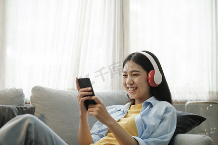 手机听音乐摄影照片_年轻的亚洲女性在家使用智能手机听音乐。