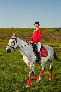 年轻的女骑手，穿着红色的 redingote 和白色的马裤，她的马在夕阳的余晖下。