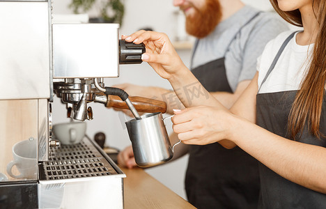咖啡业务概念-站在咖啡馆时，女咖啡师穿着围裙准备和蒸牛奶，与她的伴侣一起点咖啡。