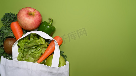 健康绿色环境摄影照片_绿色背景上装满新鲜蔬菜和水果的生态袋。