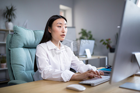 穿着现代服装在电脑前工作的韩国女商人，穿着白衬衫在键盘上打字的亚洲女性
