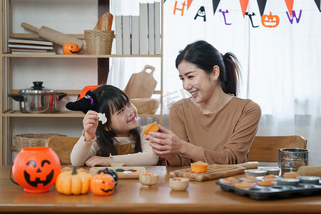 万圣节聚会摄影照片_万圣节的年轻女孩和母亲在桌上做点心和纸杯蛋糕。