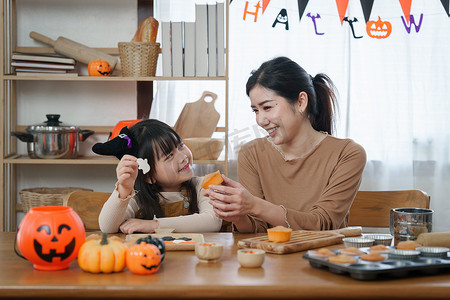 万圣节的年轻女孩和母亲在桌上做点心和纸杯蛋糕。