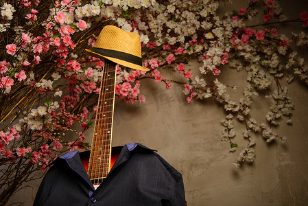 吉他穿着一件男士蓝色衬衫和一顶带指板的帽子，靠近花墙