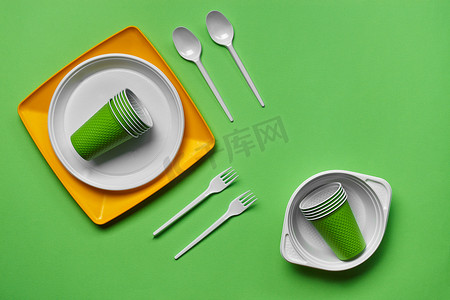 在绿色背景的五颜六色的塑料一次性餐具与复制空间。