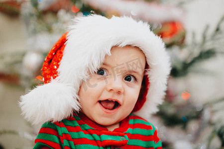 圣诞树上戴着圣诞老人帽子的小男孩非常可爱的肖像灯光背景散景。