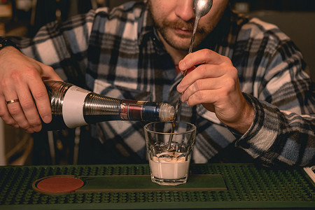 将低价摄影照片_调酒师在准备鸡尾酒白俄罗斯时将咖啡利口酒倒入加奶油的玻璃杯中