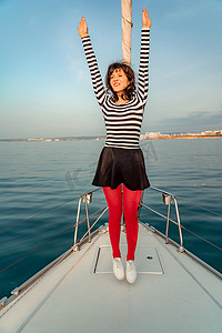 阳光明媚的夏日，女人站在游艇的鼻子上，微风吹拂着头发，背景是美丽的大海