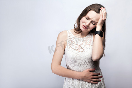 有雀斑和白色连衣裙和智能手表与银灰色背景胃痛的女人。