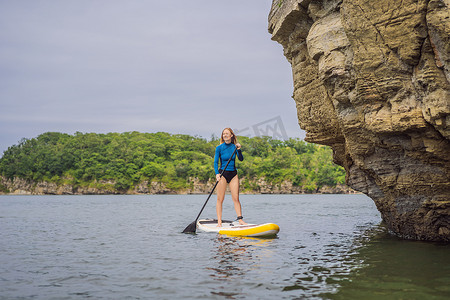 开心的年轻女性站起来在海里划桨。 