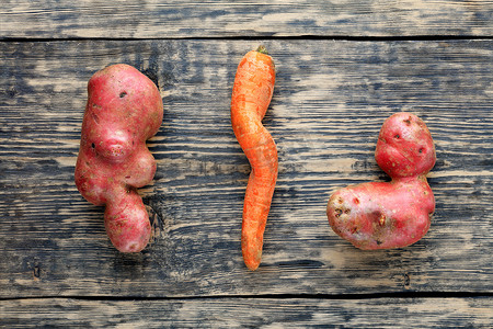 胡萝卜土豆摄影照片_旧风化木质背景上的丑陋的土豆和扭曲的胡萝卜。