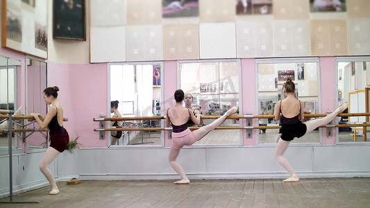 在舞厅里，年轻的芭蕾舞演员穿着黑色紧身衣，穿着足尖鞋，优雅地站在芭蕾舞课镜子前的把杆附近。