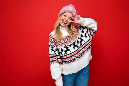 美丽的冬天二摄影照片_年轻积极快乐的美丽金发女士的照片，带着真诚的情感，戴着粉色针织帽和冬季套头衫，在红色背景中与空旷的空间隔开