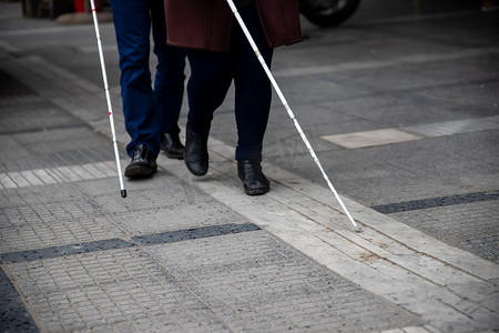 关注盲人摄影照片_盲人男女使用白色步行器在街上行走