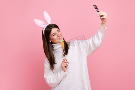 滑稽女孩的侧视肖像，兔子耳朵流淌，或者手里拿着胡萝卜进行视频通话。