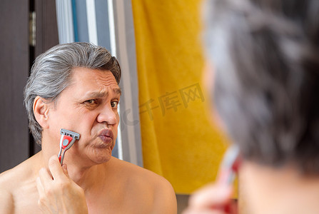 一个成年白发男子在镜子前用剃刀刮胡子