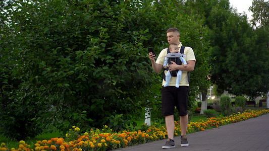 一位年轻的爸爸带着一个坐在袋鼠背包里的孩子散步。