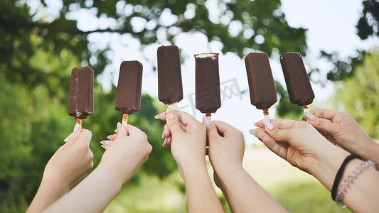 朋友们连续拿着一根棍子上的巧克力冰淇淋。
