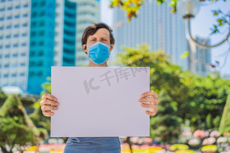 免费蓝色海报摄影照片_戴医用口罩的男子可预防冠状病毒疾病，手上拿着一张免费题词的海报。