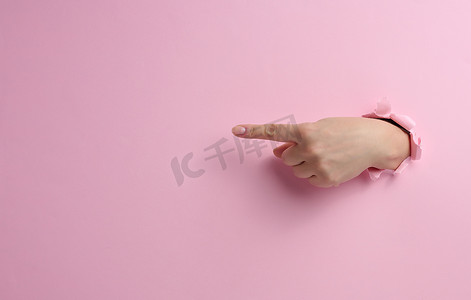 女手从粉色纸背景的破洞中伸出，身体的一部分用食指指向侧面
