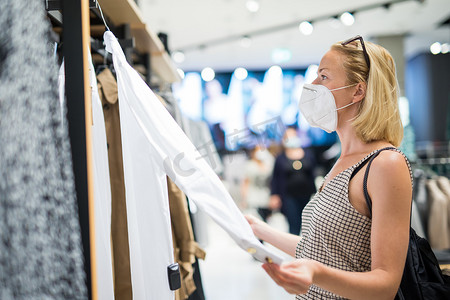 穿着防护面罩的时尚女性在零售店重新开张购物。