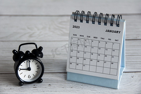 2023 年 1 月白色台历，黑色闹钟指向木桌上的 9 点钟。