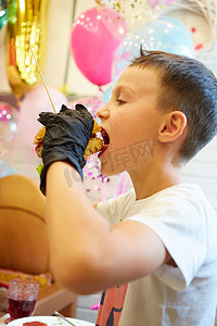 英俊的小男孩戴着黑色橡胶手套吃汉堡。