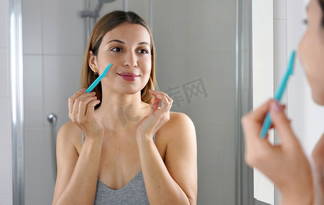 美丽的女人在家里用剃刀刮脸。