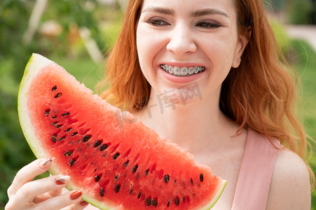 夏天，红发美女戴着牙套微笑，准备在户外吃一片西瓜