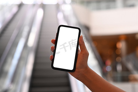 手机购物商城摄影照片_背景模糊自动扶梯的女性手持模拟手机的近景
