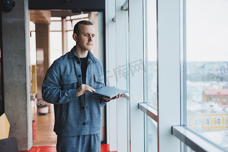 一个聪明聪明的男性经理的肖像，他拿着一台笔记本电脑在办公室进行研究，一个穿着优雅衣服的商人在触摸板上玩。