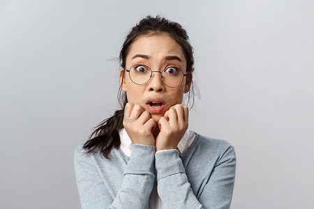 特写肖像惊慌失措，害怕的年轻亚洲女性心脏传来可怕的坏消息，双手压在脸上，喘着粗气，张开嘴，说哦，我的天哪，盯着相机害怕，灰色背景