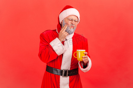 穿着圣诞老人服装、留着灰胡子的老人在喝热或冷饮料后牙齿疼痛的肖像。