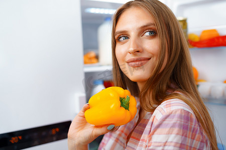 一位年轻金发女子从冰箱里拿食物的画像