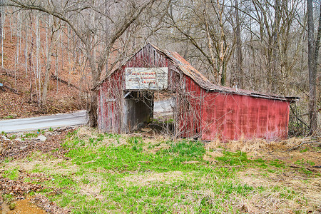 冬末路边废弃的红色谷仓，油漆褪色，路边有旧标志