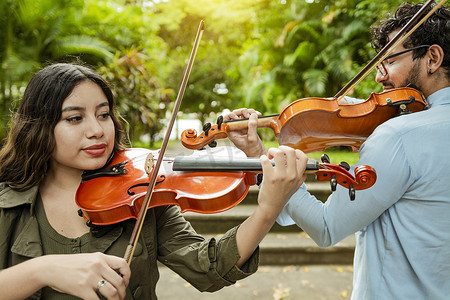 拉小提琴摄影照片_小提琴手男人和女人在户外的公园里背靠背拉小提琴。