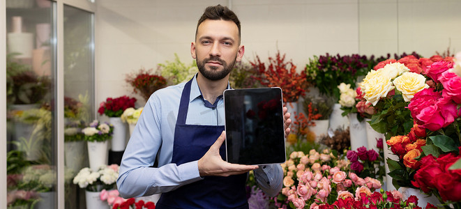 花店里的一位男花店站在花束中间，手里拿着平板电脑，屏幕朝前