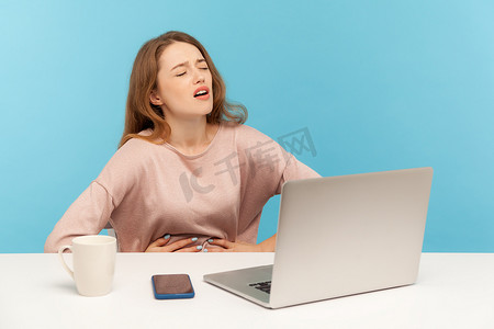 胃胀摄影照片_在蓝色背景上使用笔记本电脑的情感年轻女子。