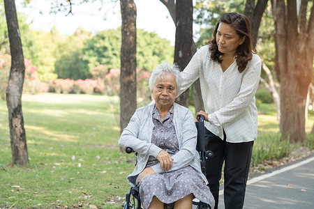 看护者帮助和照顾亚洲老年或老年老妇人病人坐在公园的轮椅上，快乐地坐在轮椅上，健康强大的医疗理念。