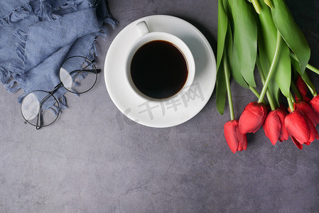 黑色的眼罩摄影照片_平面组合咖啡、郁金香花和黑色背景上的眼镜。